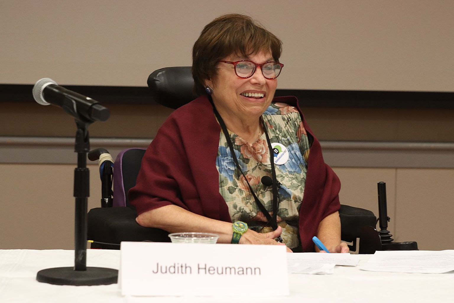 Judy Heumann sentada com um microfone.
