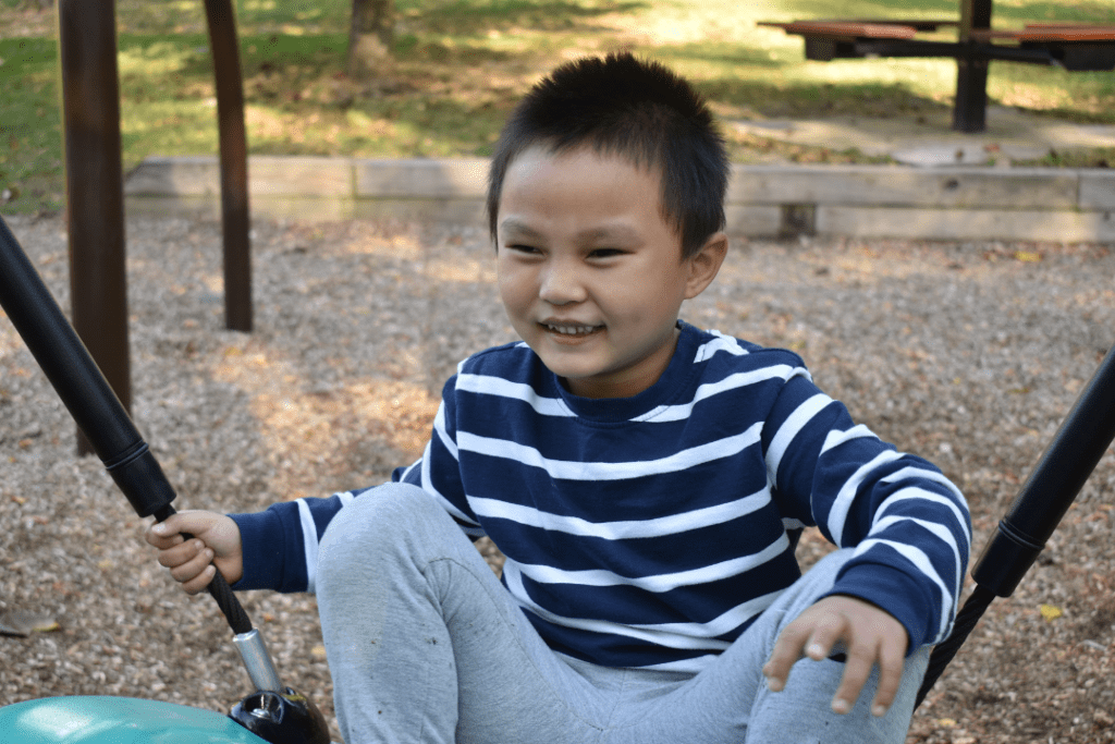 New Member Orientation: A child sits on a swing smiling.