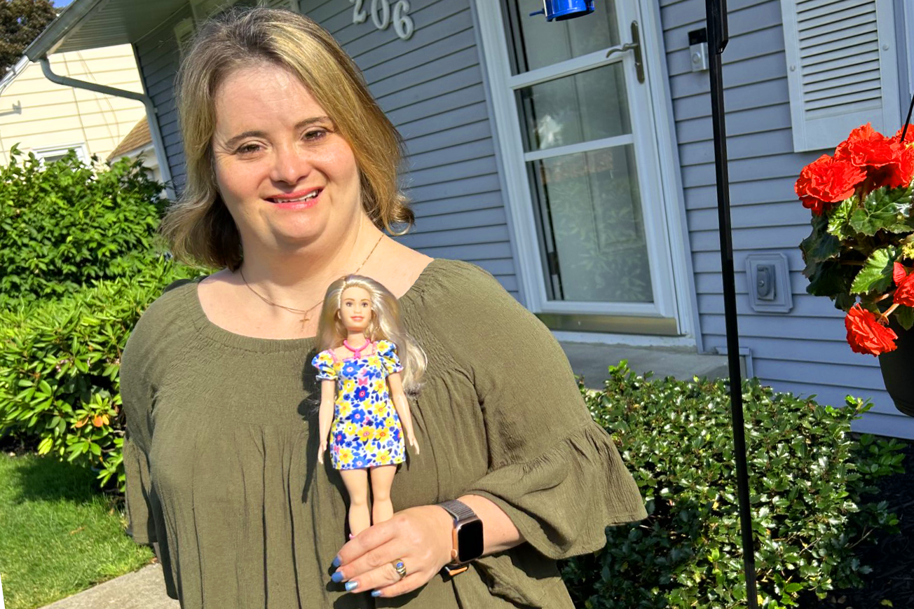 Woman with Down Syndrome holds a Barbie doll who also has Down Syndrome.