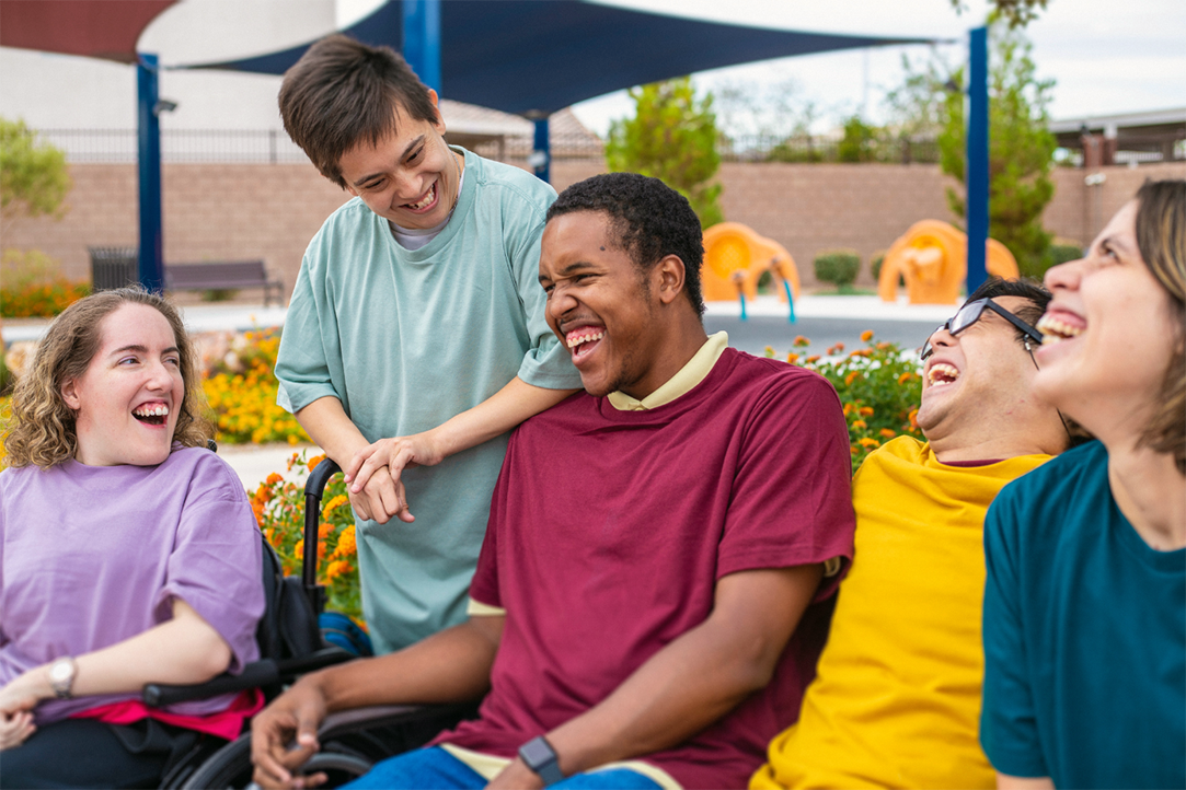 STEPS2 session: Five young people with different genders and disabilities laugh together in a park.