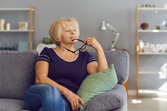 a middle aged woman is considering her decision-making options on a couch holding her glasses.