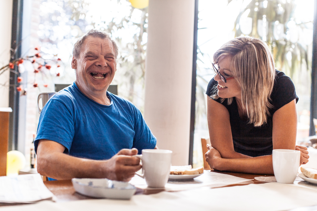 A man with IDD sits having breakfast with caregiver.