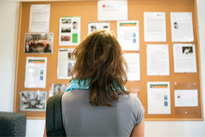 College Aspirations: A young woman stands in front of a bulletin board with many flyers posted.