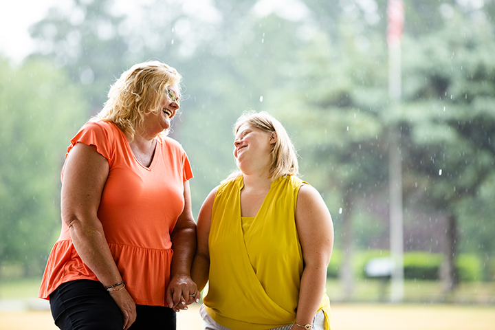 Execellence in Service: A Care Manager smiles at a young girl who has Down Syndrome outside.