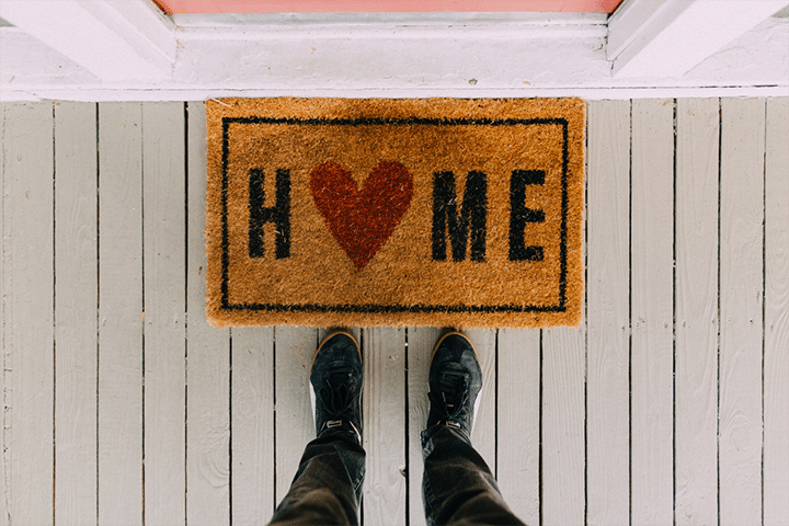 A place to call home: Two feet stand at the front of a welcome mat that says "Home" with a heart replacing the "o."