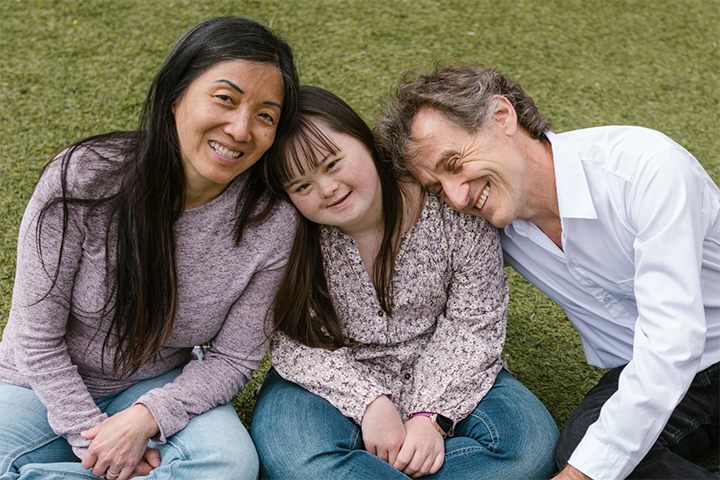 A mother sits next to her daughter who has Down syndrome and her father is at her other side.A mother sits next to her daughter who has Down syndrome and her father is at her other side.