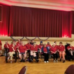 The Madison Cortland ARC Sunshine Choir A group of people with disabilities, all in red shirts, are seated together.