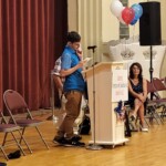 Teddy Nicholson of the Madison County Motivators, one of the largest self-advocacy groups in New York State, served as Master of Ceremonies. א יונגערמאן שטייט אויפן פאדיום ווי אנדערע קוקן אויף.